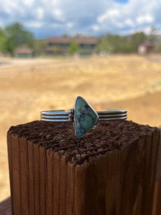 Silver cuff with a triangular Variscite stone placed on a wooden surface with a blurred outdoor background