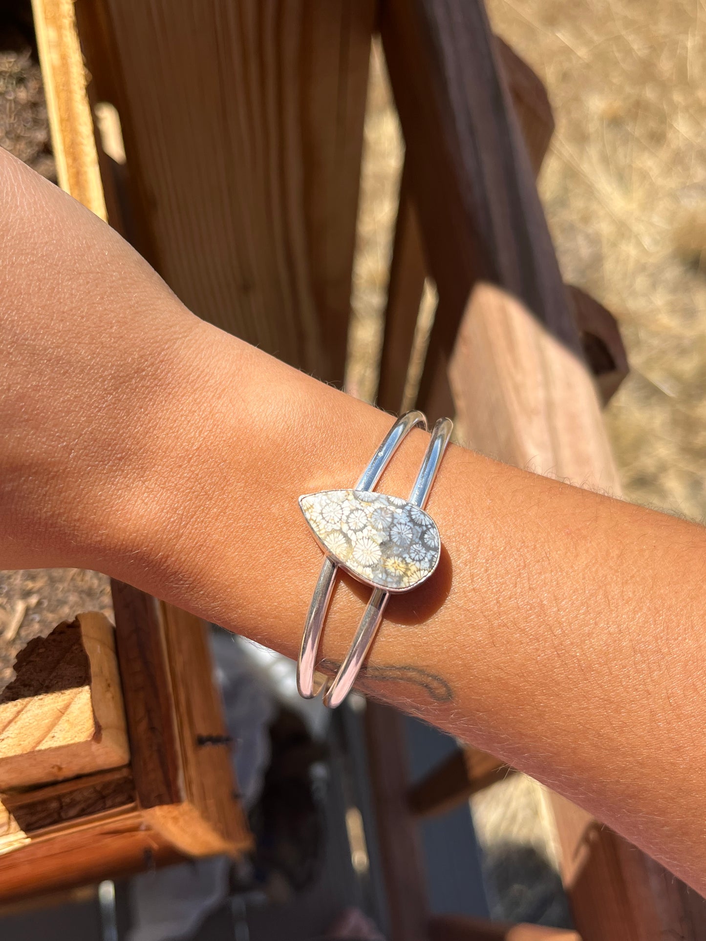 Silver teardrop Fossil Coral double band cuff bracelet on a wrist with a blurred outdoor background