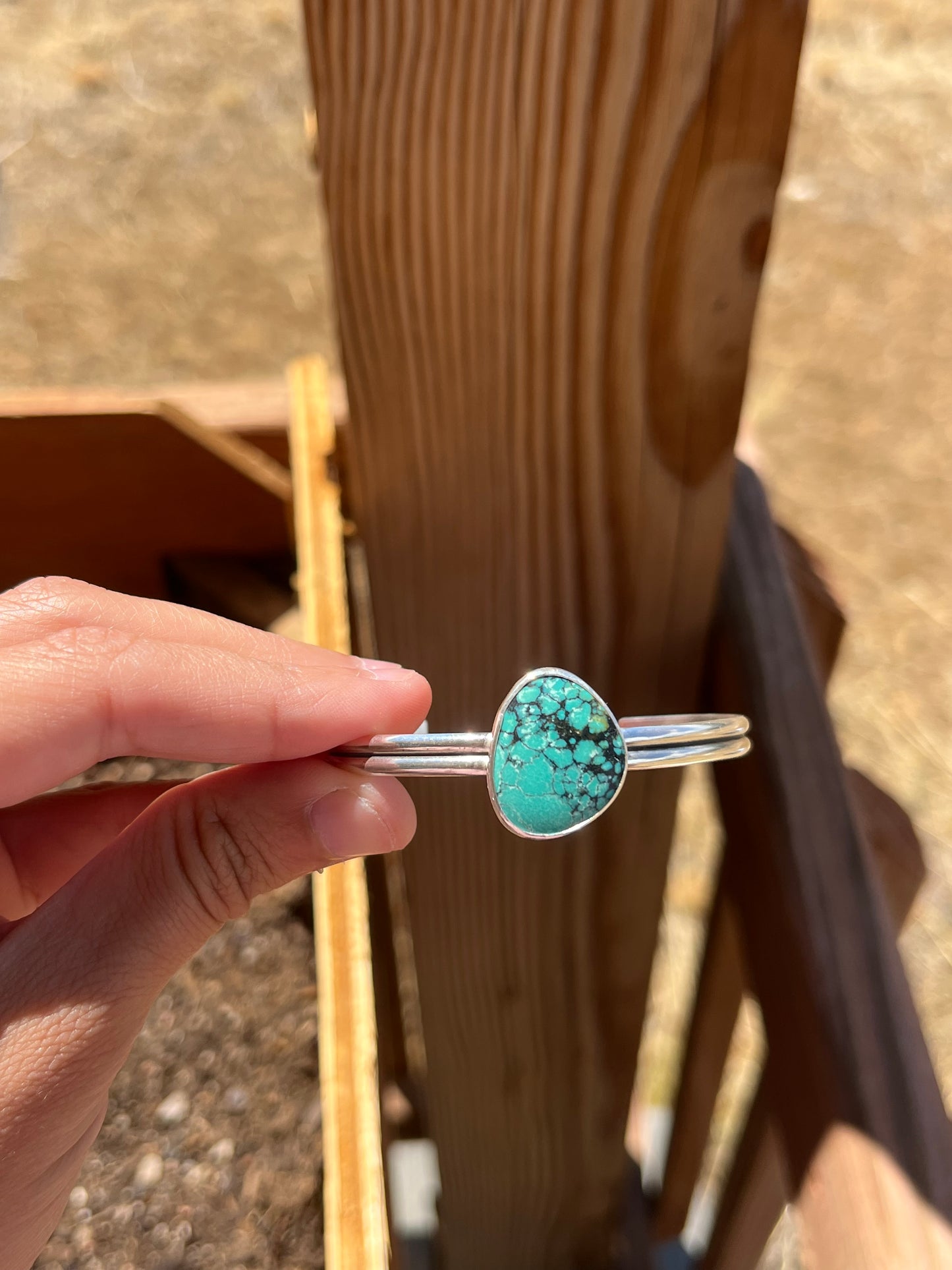 Turquoise stone bracelet held by a hand with wooden planks in the background