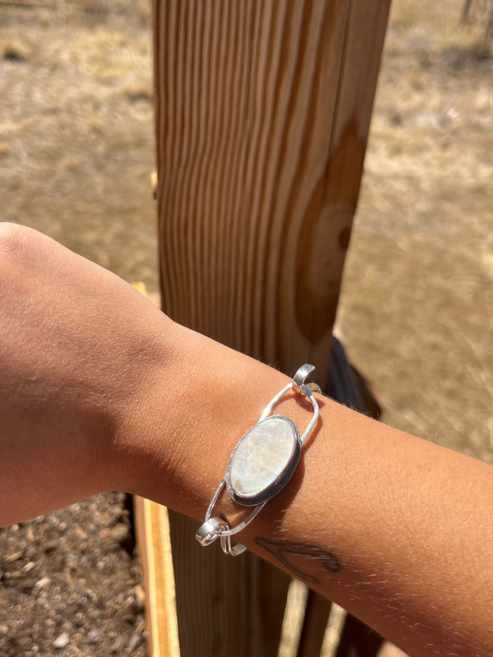 Close-up of a wrist wearing a silver bracelet with a Moonstone, against a wooden background.