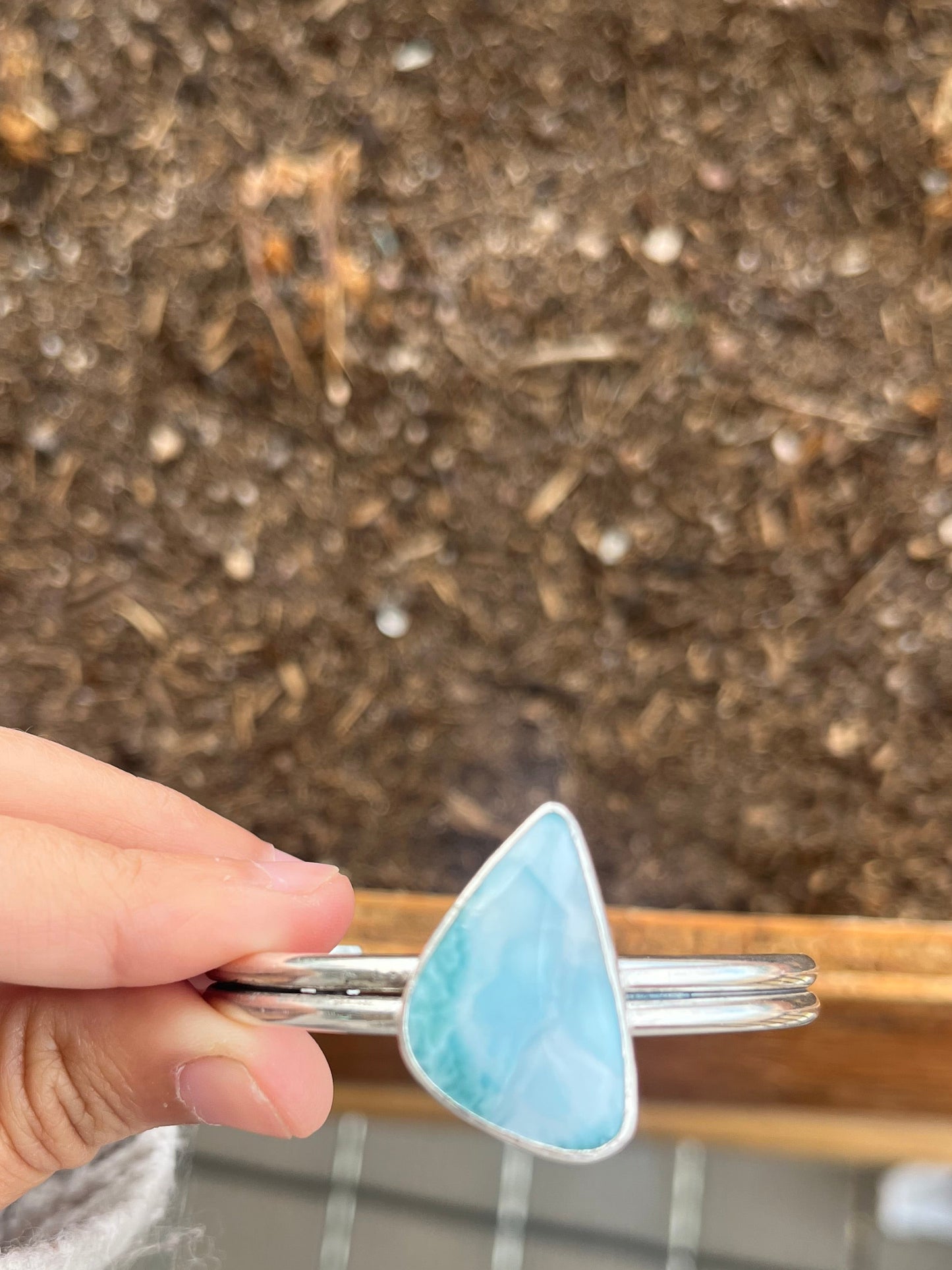 Hand holding a silver ring with a blue triangular Larimar stone against a blurred background